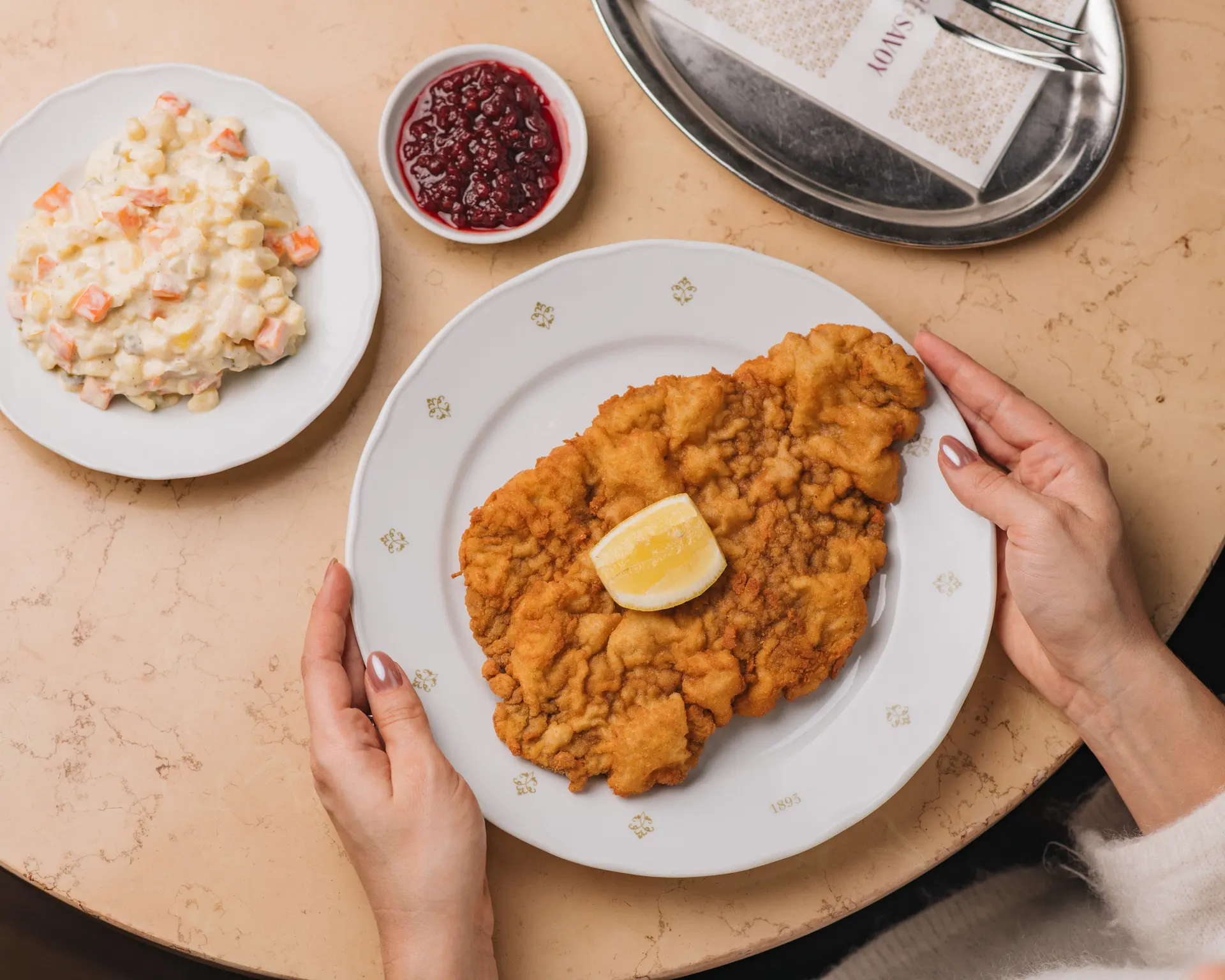 Chicken schnitzel with lemon, potato salad and cranberries served at the table.