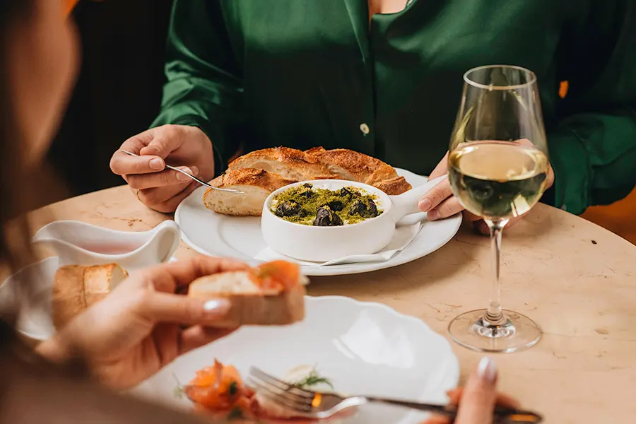 Guests sharing a starter with bread, herb sauce and white wine at the table.
